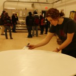 A student paints a table in the scene shop while journalism students interview theater department chair Ron Shields.